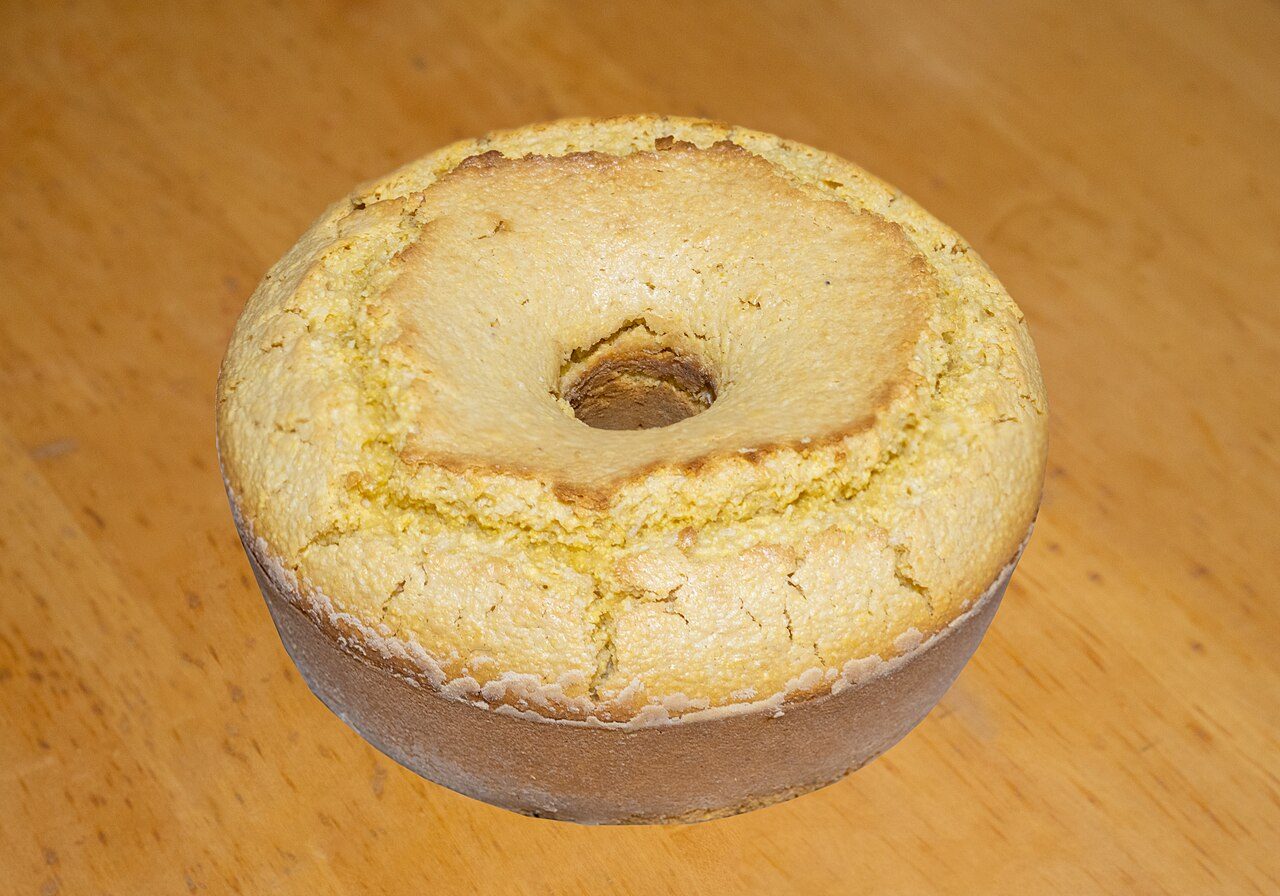 Bolo de fubá inteiro, de forma com furo, com superfície dourada e rachada, sobre mesa de madeira